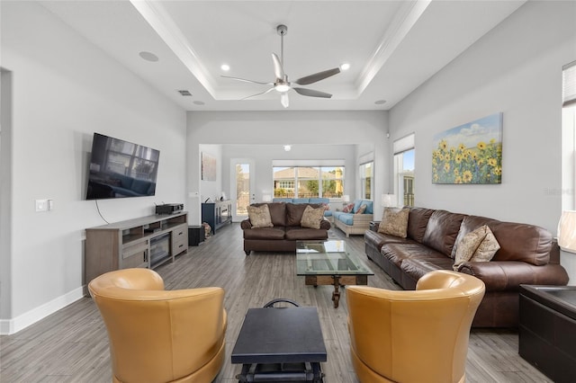 living room with a tray ceiling, ornamental molding, light wood finished floors, and ceiling fan