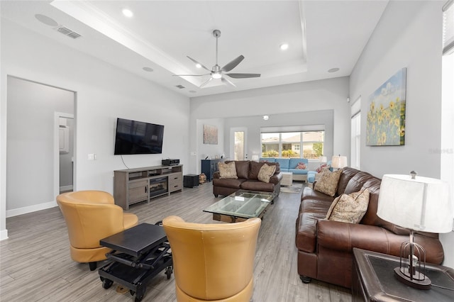 living area featuring a raised ceiling, visible vents, light wood-type flooring, baseboards, and ceiling fan