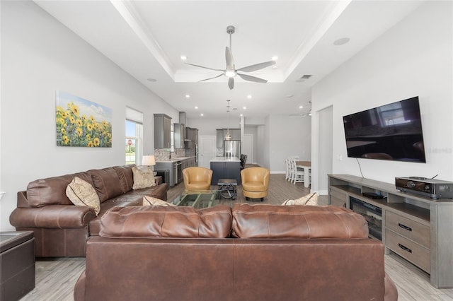 living room featuring a raised ceiling, ceiling fan, visible vents, and light wood-type flooring