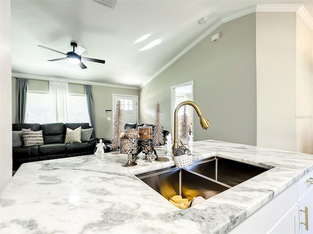 kitchen with lofted ceiling, light stone counters, ornamental molding, and a sink