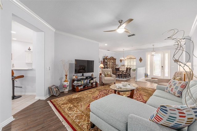 living area with wood finished floors, visible vents, ornamental molding, baseboards, and ceiling fan with notable chandelier
