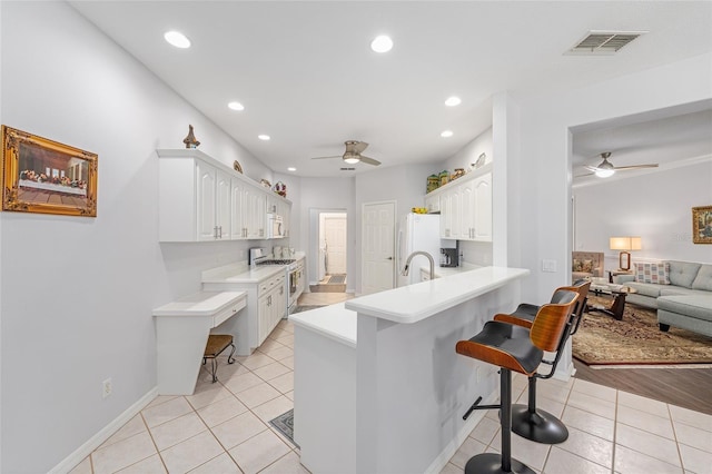 kitchen featuring visible vents, a kitchen breakfast bar, ceiling fan, and white appliances