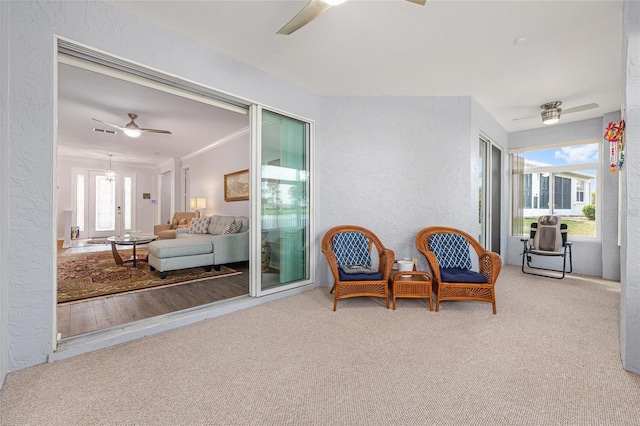 sitting room featuring a textured wall, visible vents, carpet, and ceiling fan