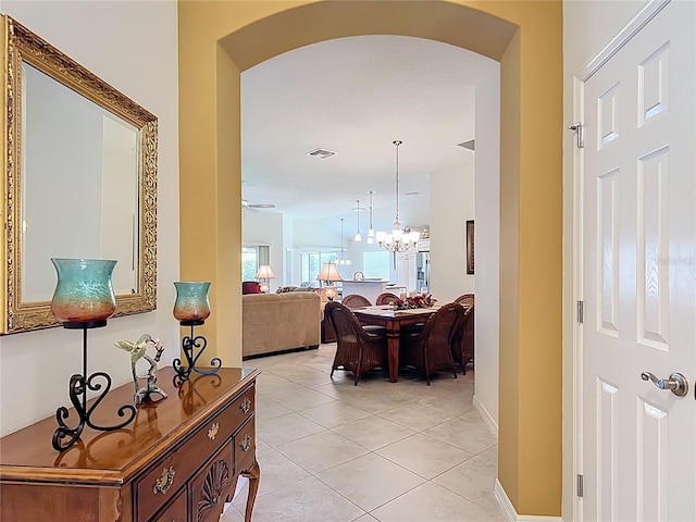 corridor featuring light tile patterned flooring, a notable chandelier, arched walkways, baseboards, and visible vents