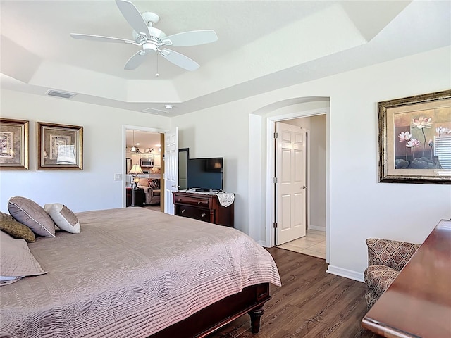 bedroom featuring a ceiling fan, visible vents, wood finished floors, a raised ceiling, and baseboards