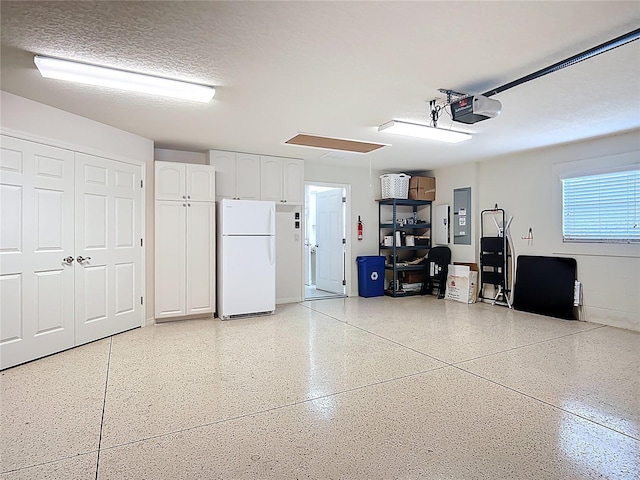 garage with a garage door opener, freestanding refrigerator, and electric panel
