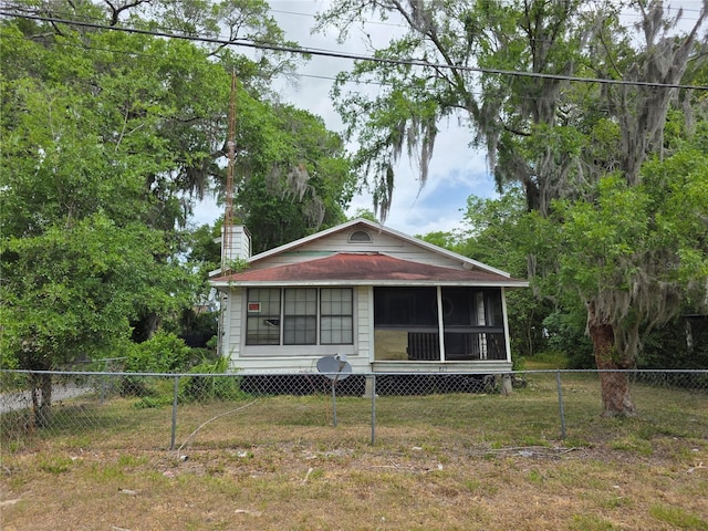 view of front of property featuring a fenced backyard, a chimney, a sunroom, and a front yard