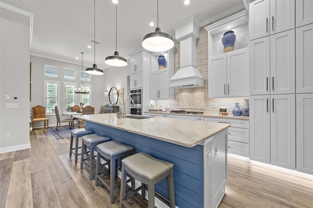 kitchen featuring a kitchen island with sink, stainless steel appliances, light wood finished floors, baseboards, and ornamental molding