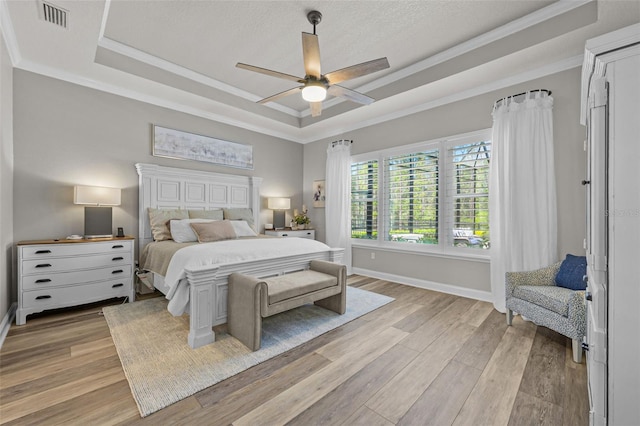 bedroom with light wood-type flooring, a tray ceiling, baseboards, ornamental molding, and visible vents