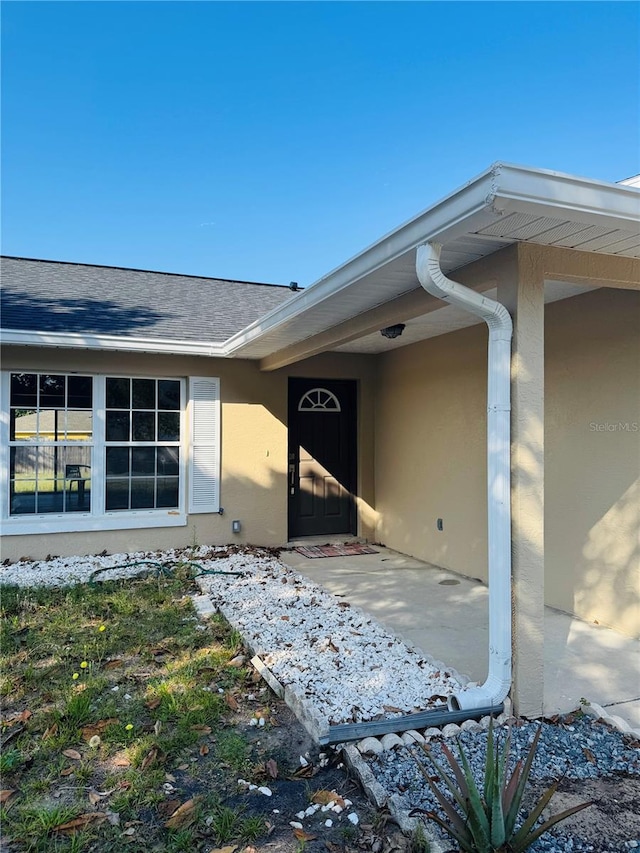 doorway to property with a shingled roof and stucco siding