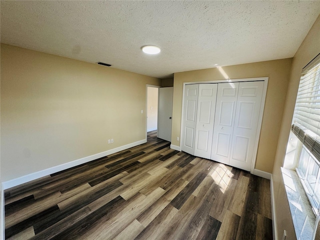 unfurnished bedroom featuring a closet, visible vents, baseboards, a textured ceiling, and wood finished floors