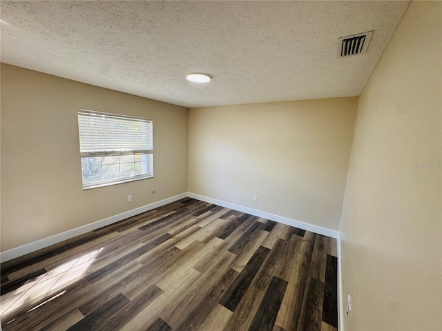 unfurnished room with a textured ceiling, visible vents, dark wood-style floors, and baseboards