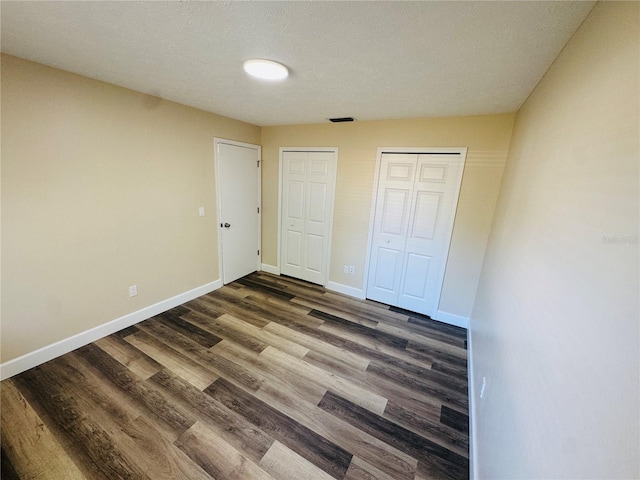 unfurnished bedroom featuring a closet, dark wood-style flooring, visible vents, and baseboards