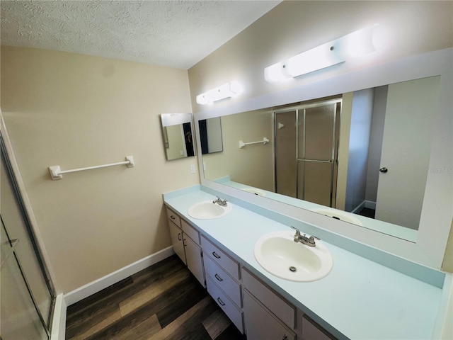 bathroom with wood finished floors, a shower stall, double vanity, and a sink