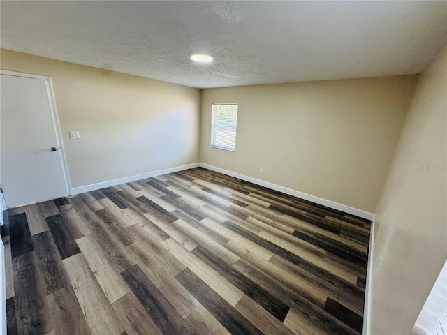 empty room with dark wood-style flooring, a textured ceiling, and baseboards