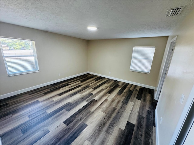 unfurnished room featuring a textured ceiling, visible vents, and dark wood finished floors