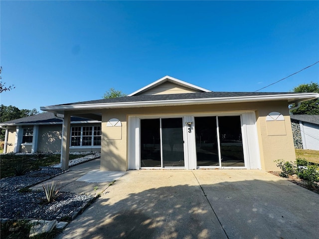 rear view of house featuring a shingled roof, stucco siding, and a patio area