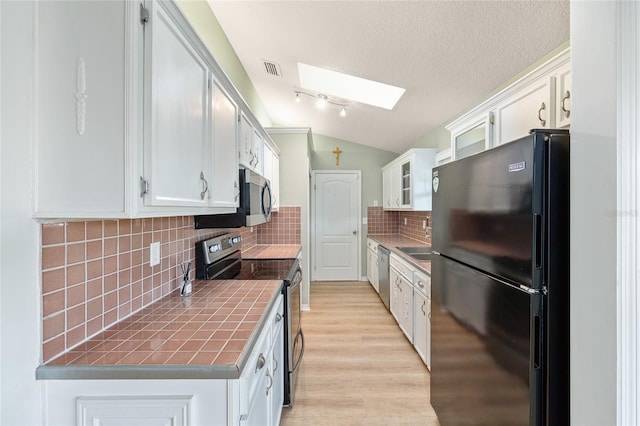 8 Banyan Dr, Ocala, FL 34472 - kitchen featuring tile countertops, lofted ceiling with skylight, white cabinets, and stainless steel appliances