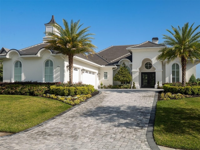 mediterranean / spanish house featuring a front yard, a garage, decorative driveway, stucco siding, and french doors
