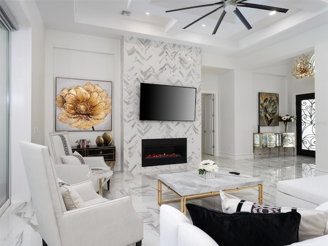 living area with a ceiling fan, a tray ceiling, and marble finish floor