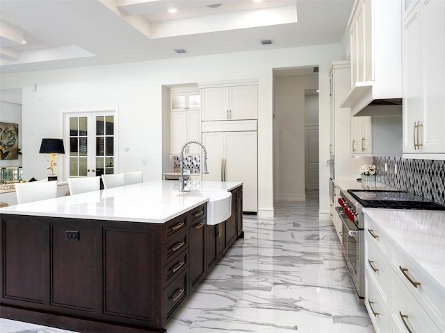 kitchen with premium appliances, a raised ceiling, white cabinets, and a sink