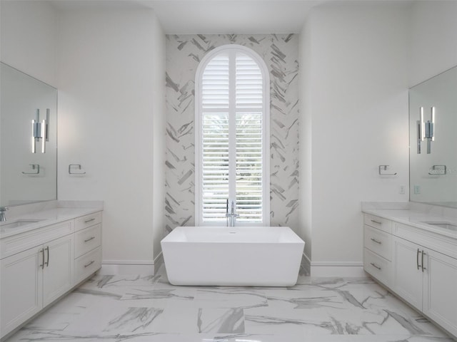 bathroom featuring marble finish floor, a healthy amount of sunlight, a soaking tub, and two vanities
