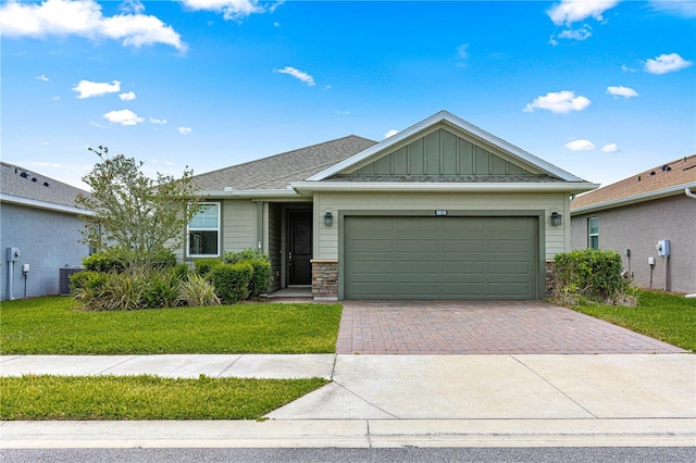 single story home with a front yard, a garage, stone siding, decorative driveway, and board and batten siding