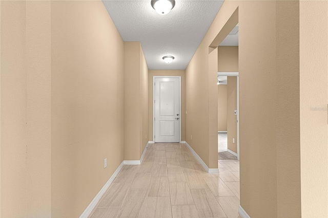 hall with a textured ceiling and baseboards