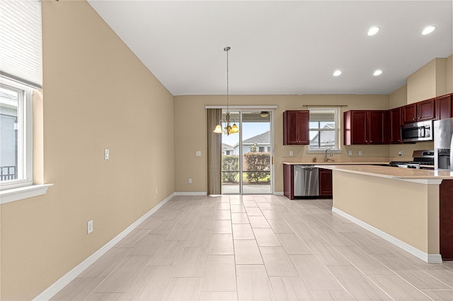 kitchen with a sink, appliances with stainless steel finishes, light countertops, baseboards, and a notable chandelier