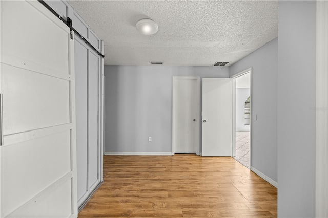 14171 SW 8th Ave, Ocala, FL 34473 - unfurnished bedroom with a textured ceiling, a barn door, and light wood-style floors