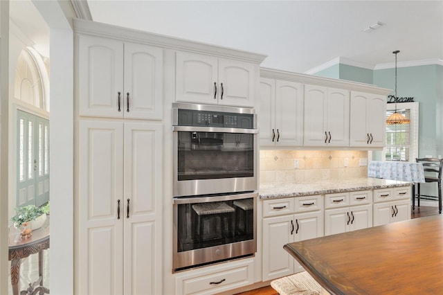 kitchen with crown molding, stainless steel double oven, light stone countertops, decorative light fixtures, and backsplash