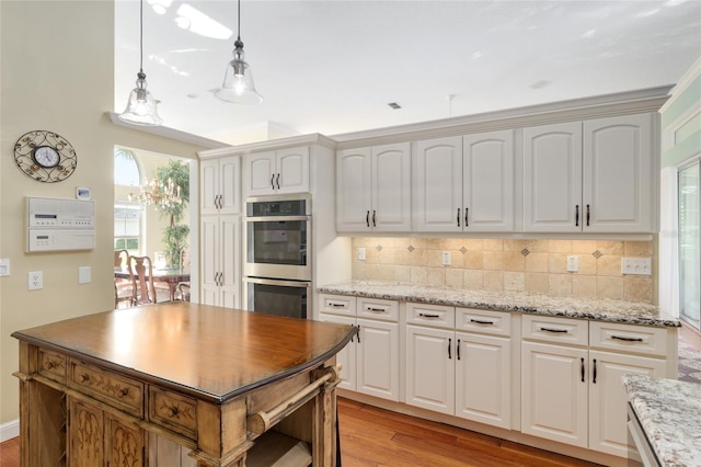 kitchen featuring pendant lighting, tasteful backsplash, light wood-style floors, stainless steel double oven, and light stone countertops