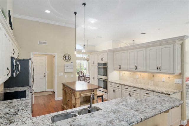 kitchen with a sink, appliances with stainless steel finishes, visible vents, light stone countertops, and backsplash