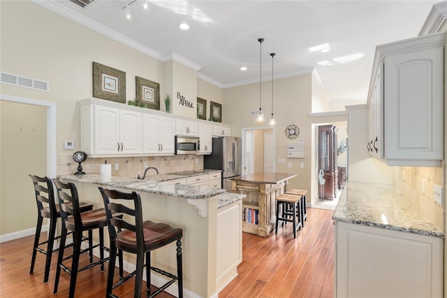 kitchen featuring a kitchen breakfast bar, visible vents, stainless steel appliances, light wood-style floors, and a peninsula