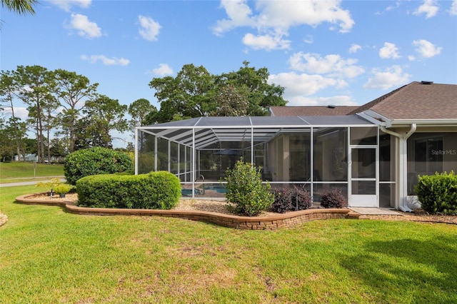 rear view of house featuring glass enclosure, a yard, and roof with shingles