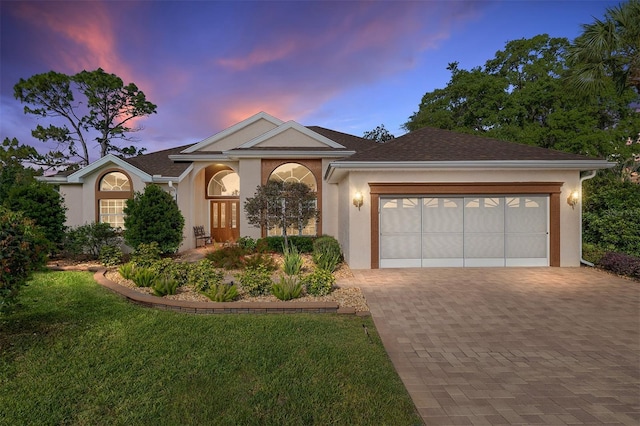 single story home with stucco siding, decorative driveway, a lawn, and a garage