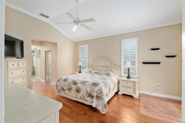 bedroom with light wood finished floors, crown molding, visible vents, vaulted ceiling, and baseboards