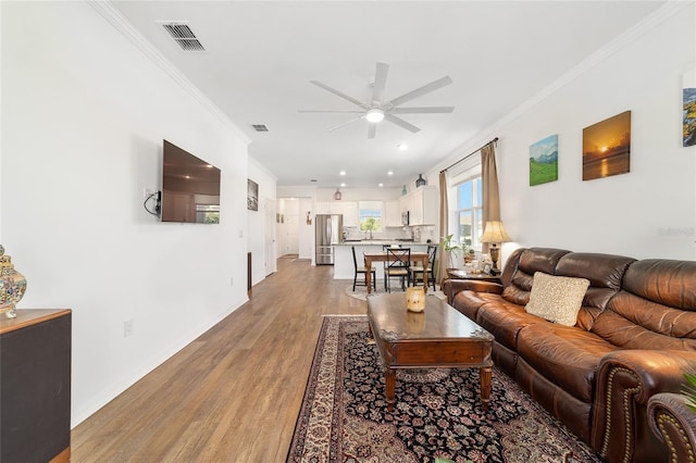 living room with ceiling fan, light wood finished floors, ornamental molding, baseboards, and recessed lighting