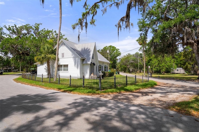 view of property exterior with metal roof, driveway, a yard, and a fenced front yard