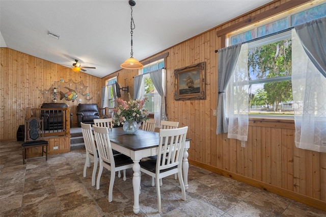 dining space featuring a ceiling fan, visible vents, wood walls, and stone finish flooring