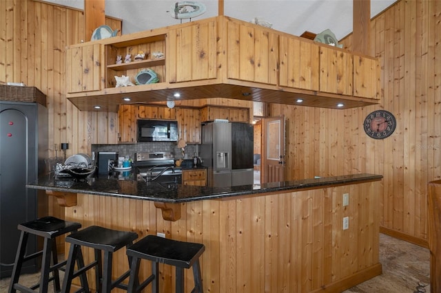 kitchen with tasteful backsplash, a peninsula, appliances with stainless steel finishes, a sink, and wooden walls