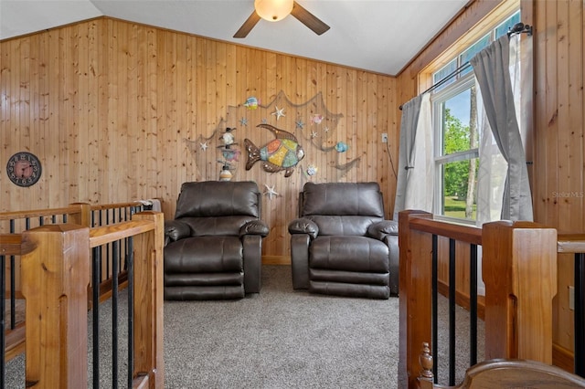 sitting room featuring an upstairs landing, a ceiling fan, wood walls, and carpet floors