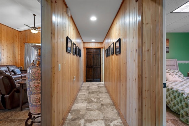 hall with baseboards, wooden walls, and stone finish floor