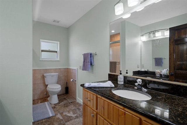 bathroom featuring tile walls, vanity, toilet, a wainscoted wall, and visible vents