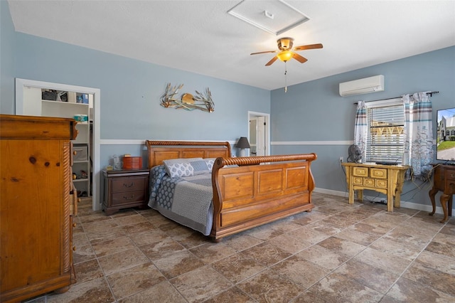 bedroom featuring baseboards, stone finish flooring, a wall unit AC, and a walk in closet