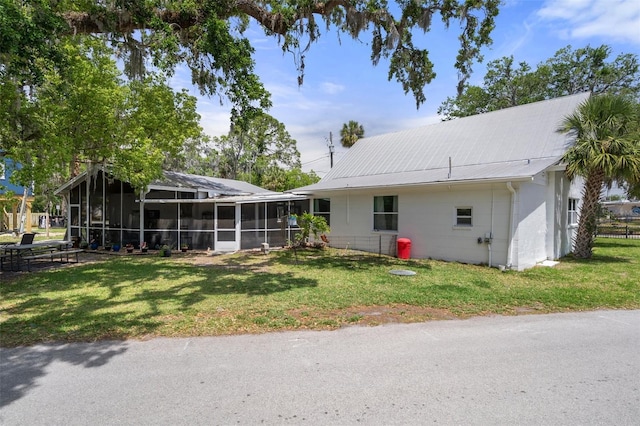 rear view of house with concrete block siding, metal roof, a sunroom, and a lawn