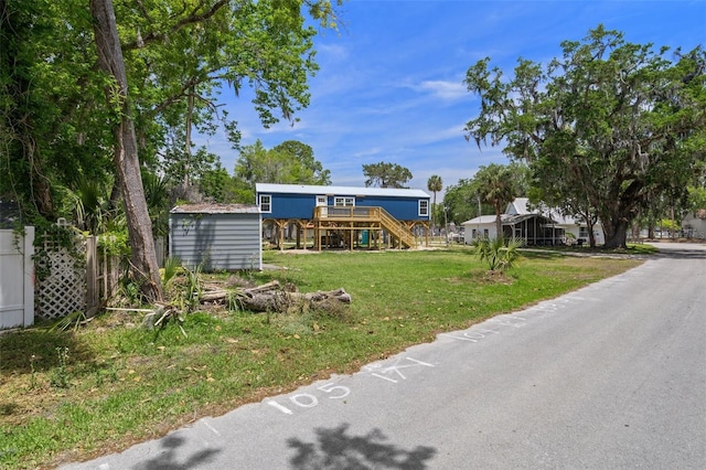 view of front of property featuring a deck, an outbuilding, a storage shed, a front lawn, and stairs