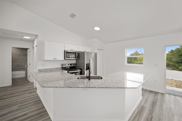 kitchen with light stone countertops, light wood-style flooring, stainless steel appliances, a sink, and a peninsula