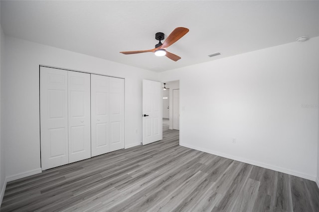 unfurnished bedroom featuring a closet, ceiling fan, visible vents, baseboards, and wood finished floors