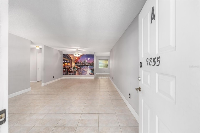 interior space featuring light tile patterned floors, baseboards, ceiling fan, and a textured ceiling